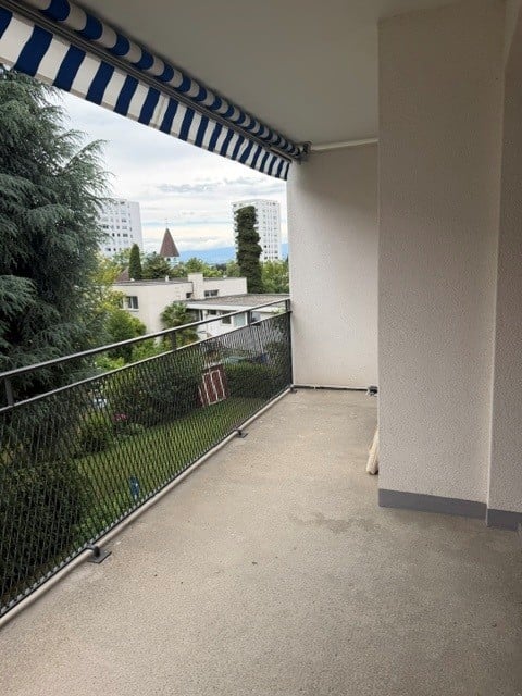 Balcony with striped awning, metal railing, and view of greenery and buildings.