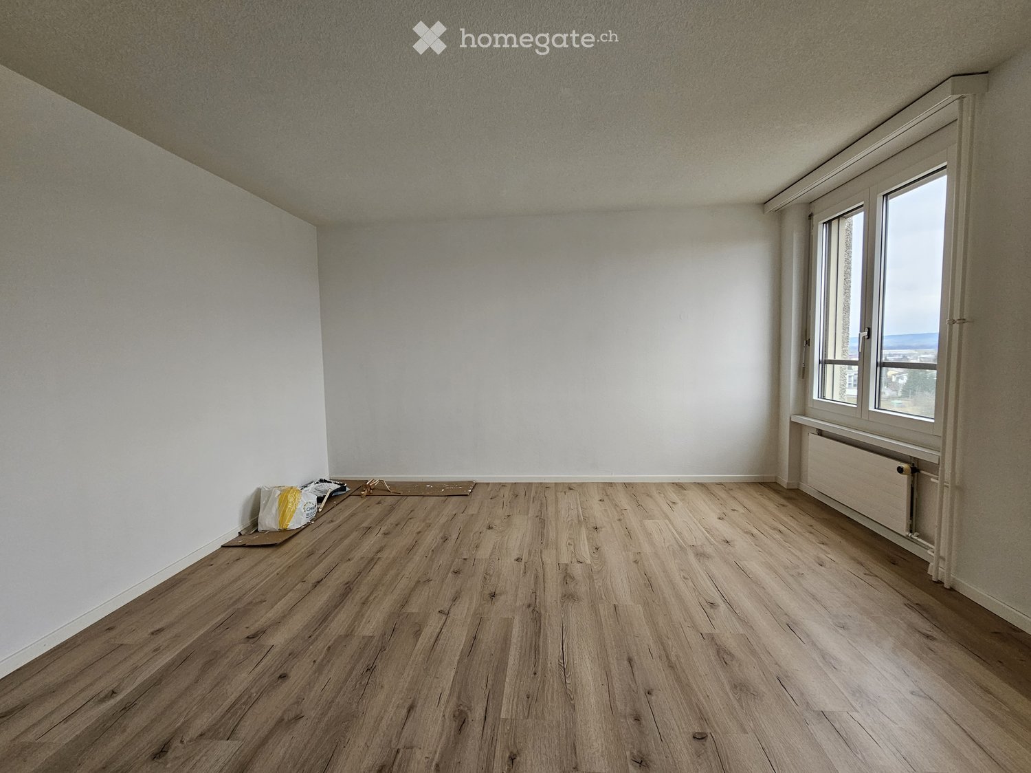 Empty room with light wooden flooring, white walls, and a large window with a view. No furniture or equipment is present.