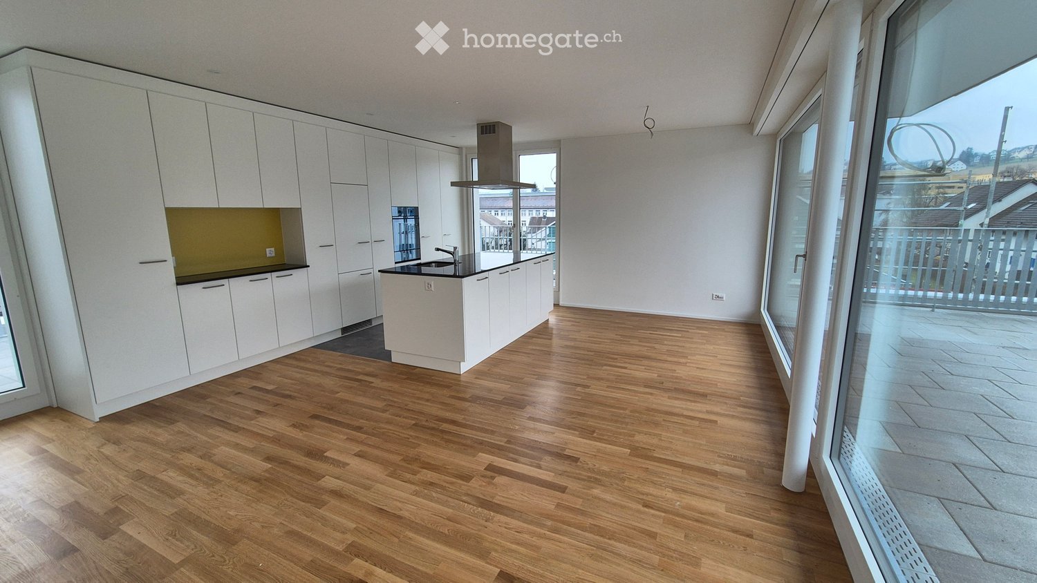 Modern kitchen with white cabinetry, wooden flooring, and large windows overlooking a balcony.