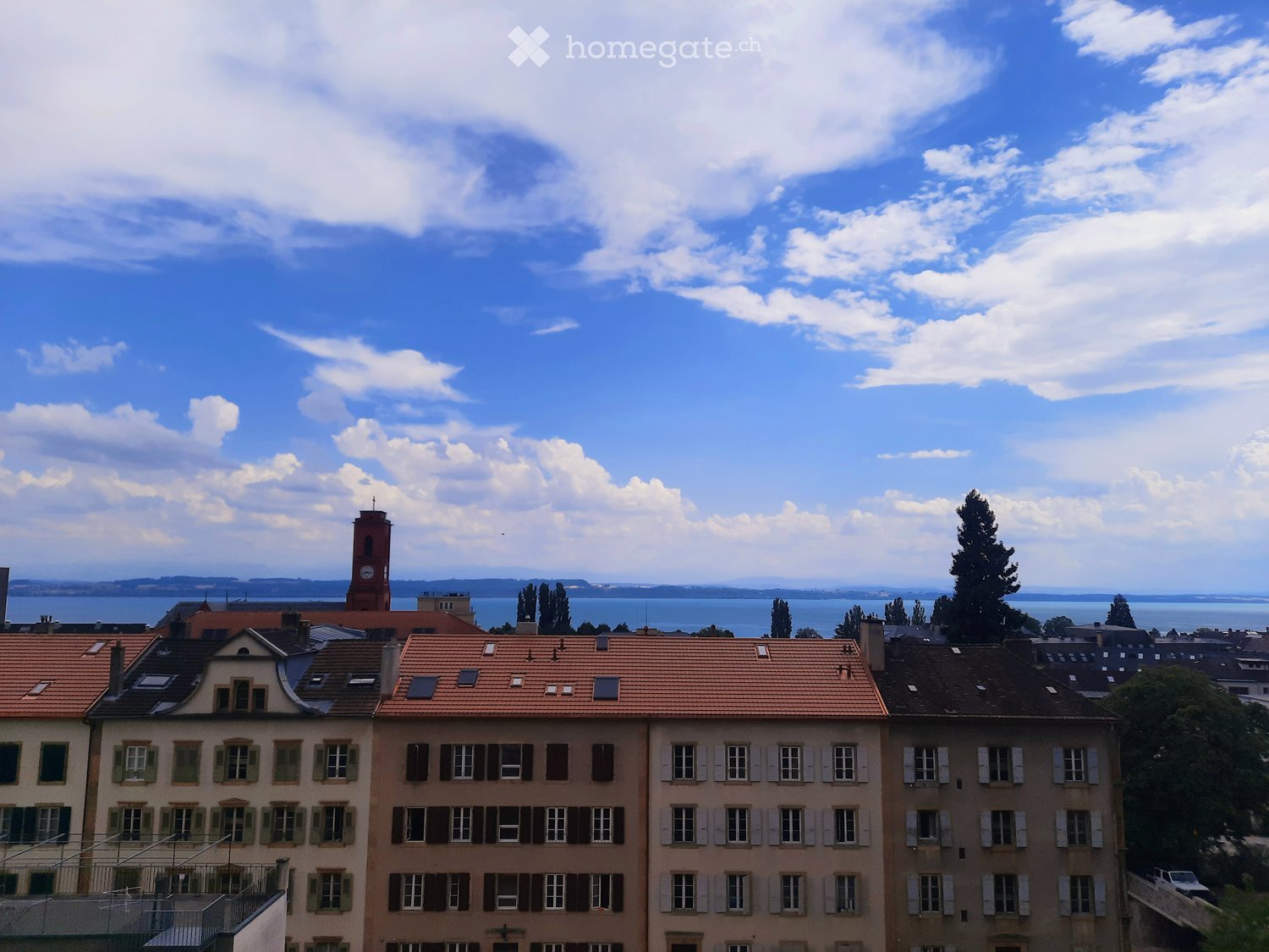 View of a cityscape with multiple buildings, red-tiled roofs, and a distant body of water.