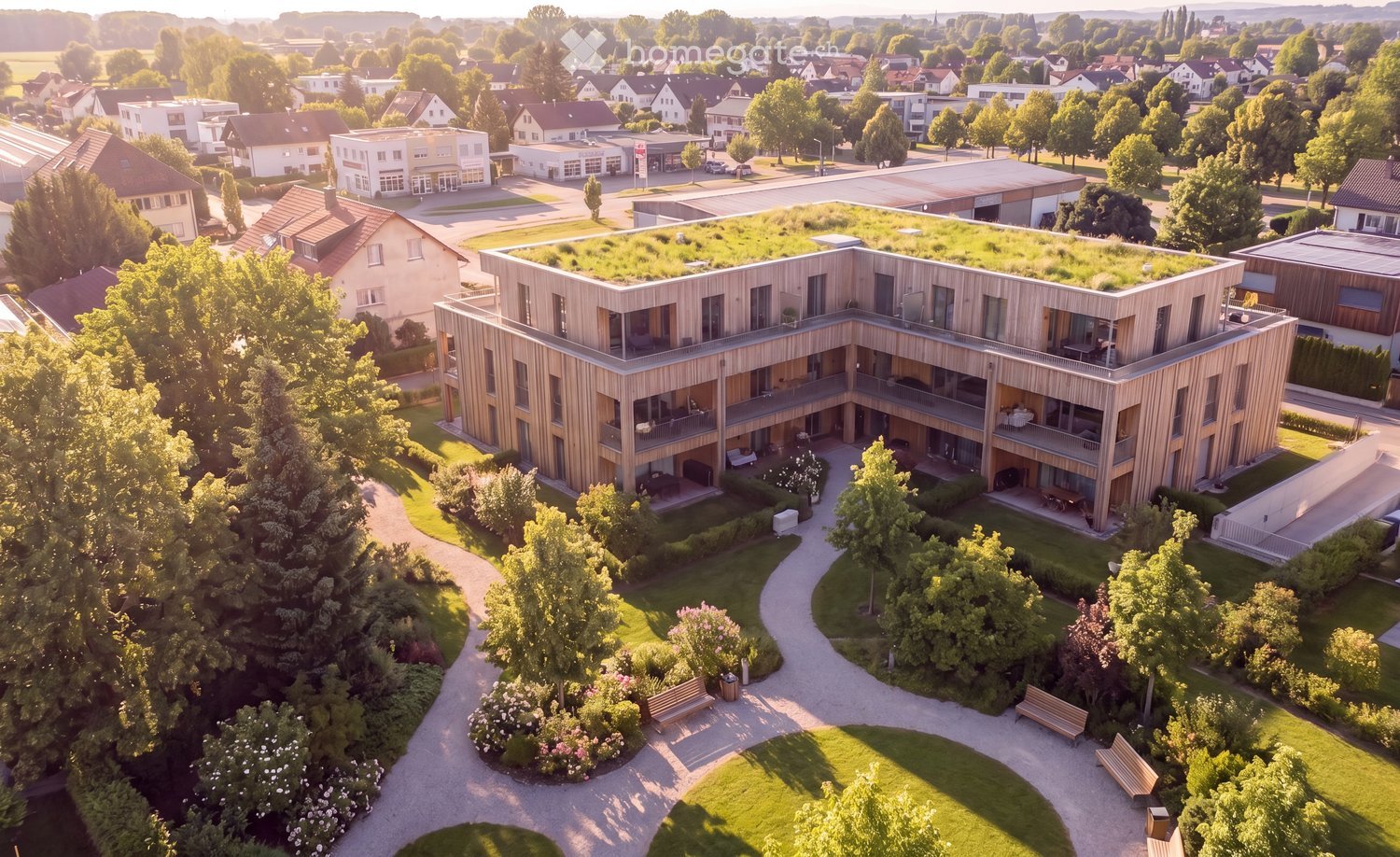 Aerial view of a modern, multi-story residential building with wooden facades and balconies, surrounded by greenery and pathways.