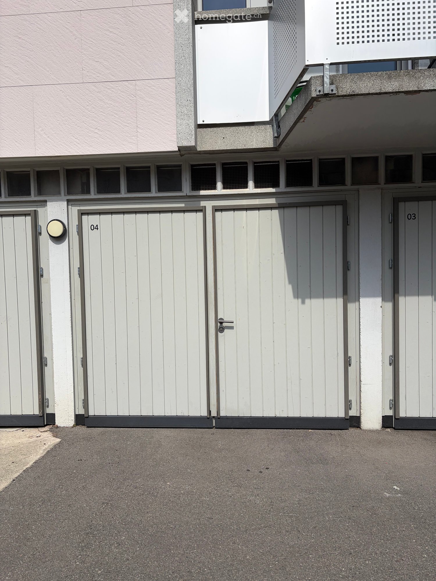 Exterior view of a building with multiple garage doors, numbered 03, 04, and others, and a small balcony area above.