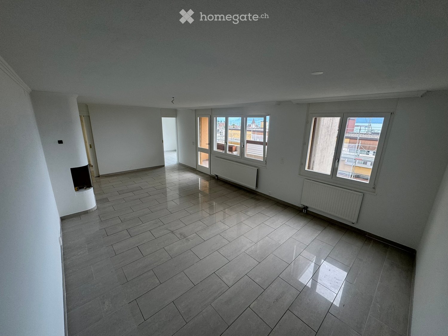 Empty room with tiled floor, white walls, large windows, and a door leading to a balcony.