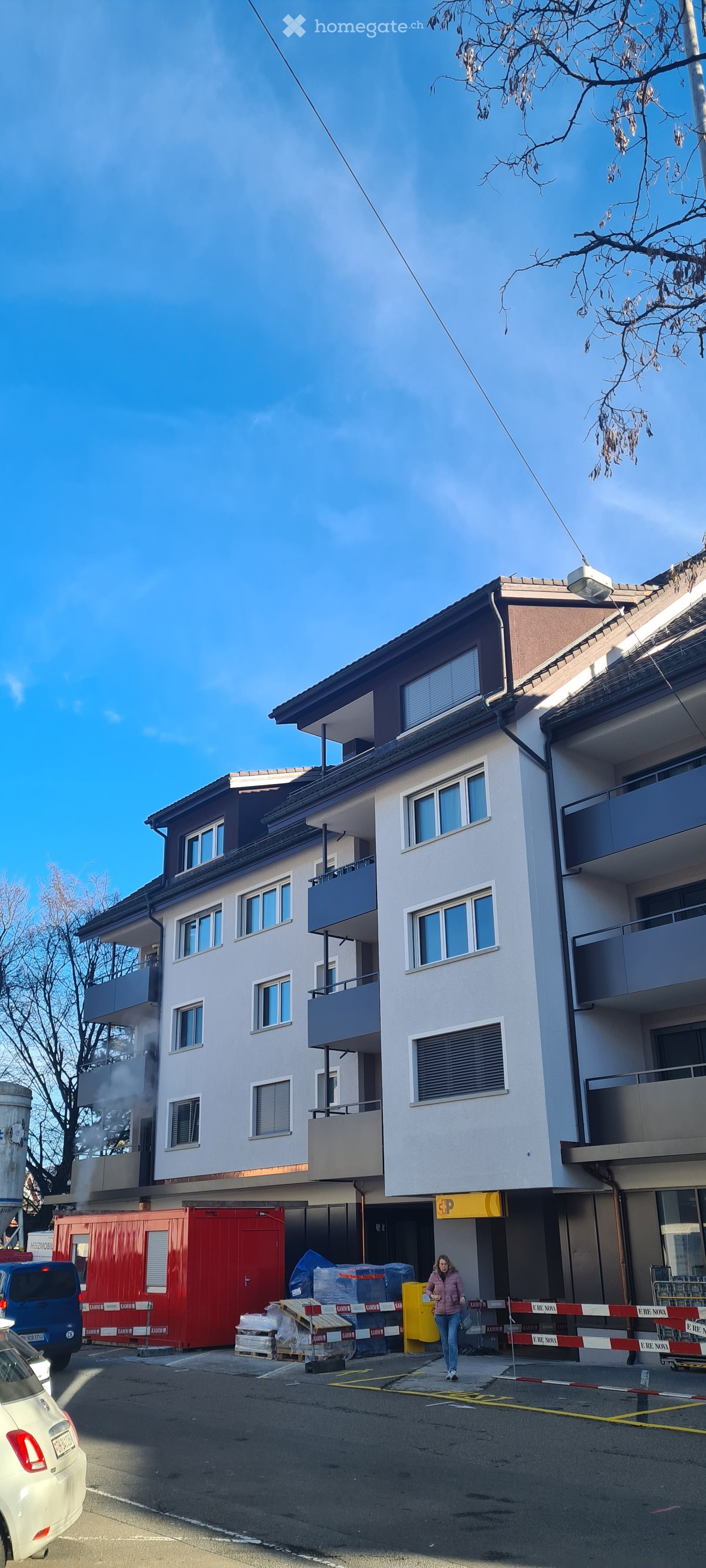 Multi-story residential building with balconies, windows, and a parking area in front.