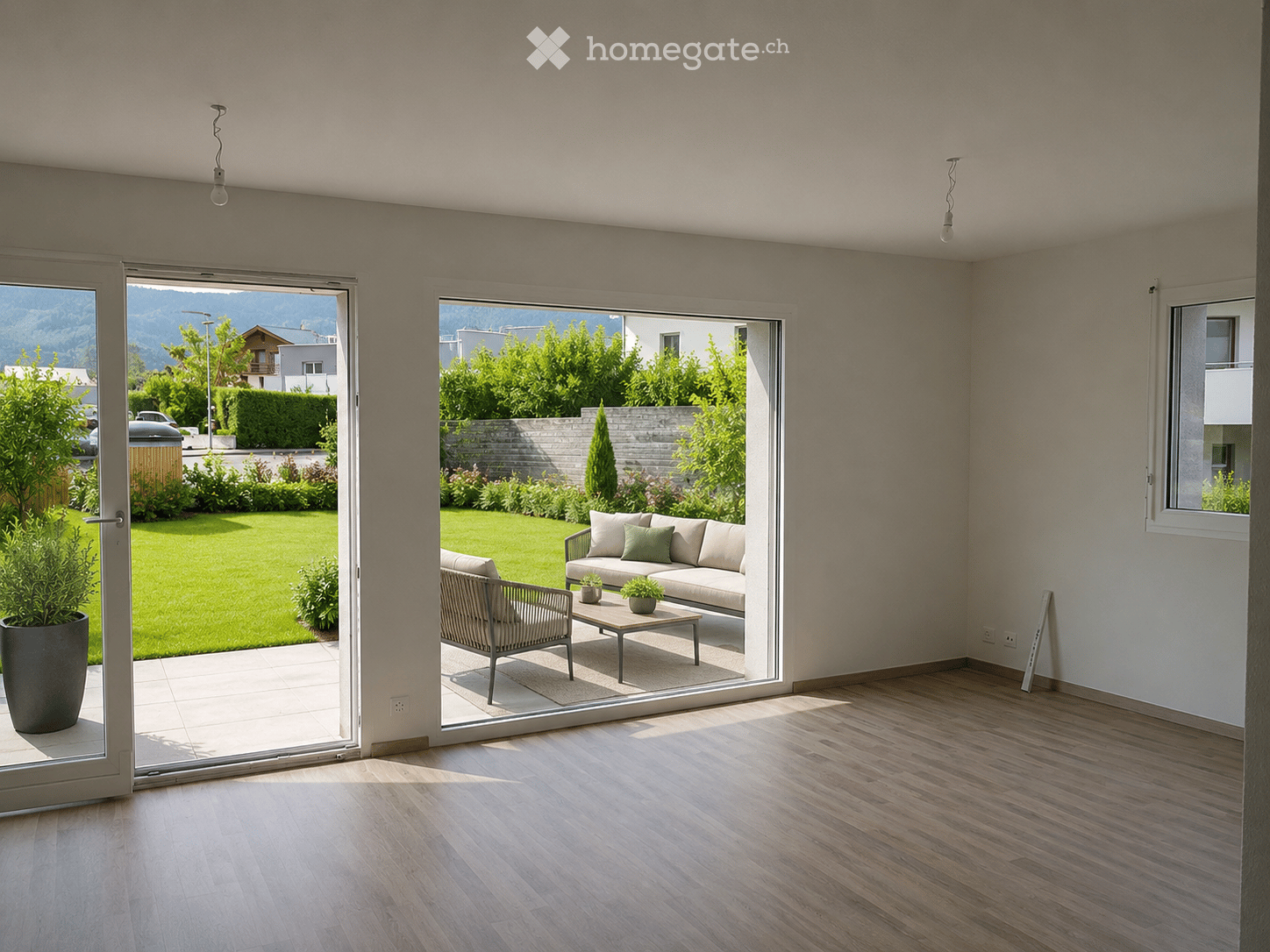 Bright living room with wooden flooring, large sliding glass doors opening to a garden, sofa, coffee table, and chair.