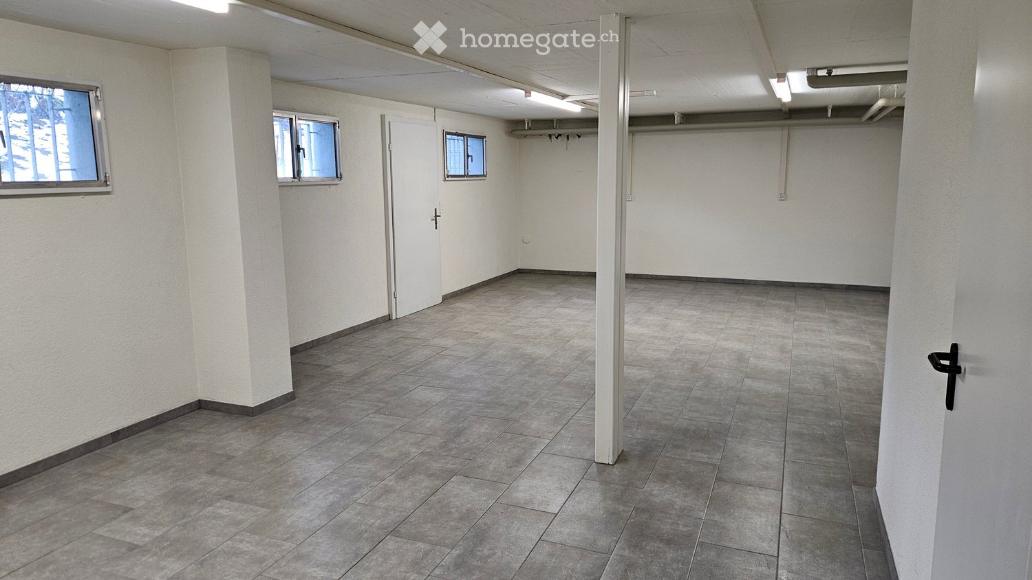 Empty room with tile flooring, white walls, and white doors. There are three small windows and recessed ceiling lighting.
