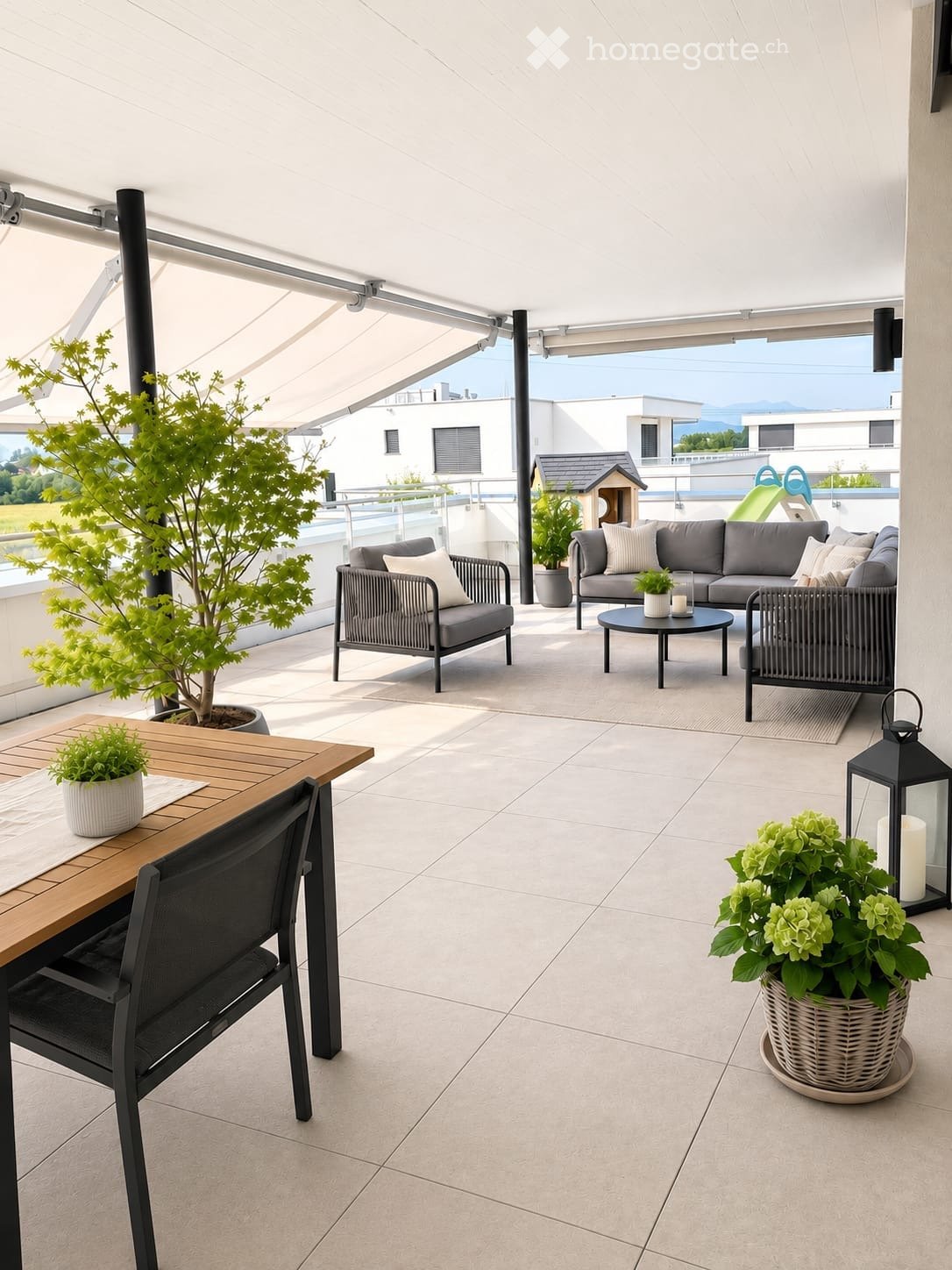 Modern balcony with tiled floor, grey sofa, wooden dining table, black chairs, and potted plants.
