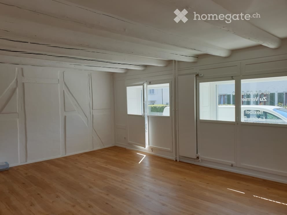 Empty room with wooden flooring, white walls, and large windows with blinds. No furniture or equipment present.