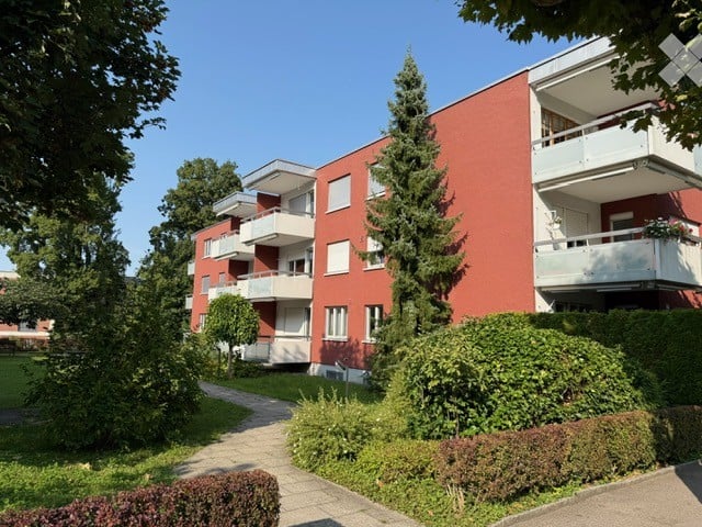 Red brick apartment building with multiple balconies and surrounding greenery.