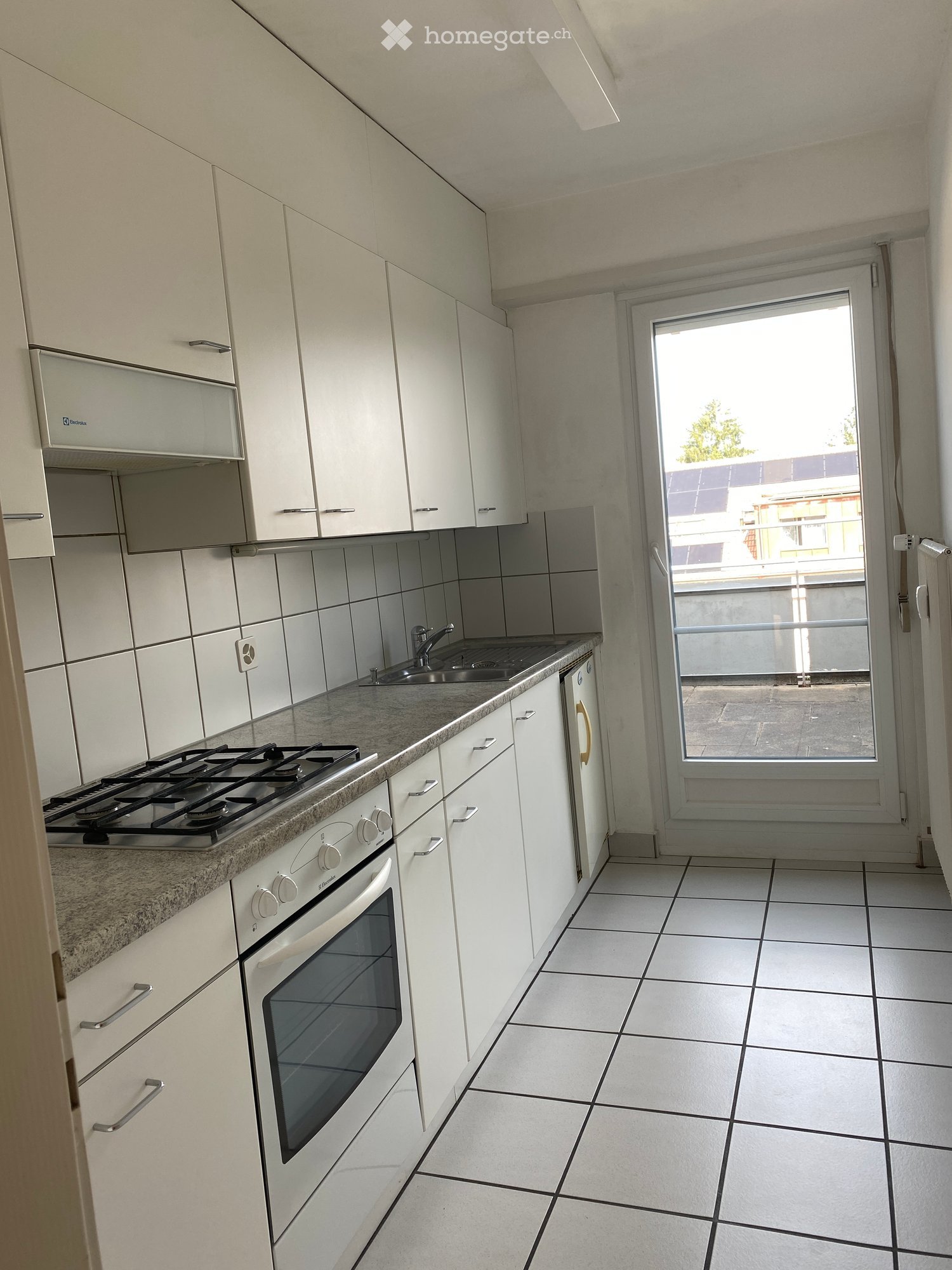 Modern kitchen with white cabinets, granite countertop, gas stove, oven, and sink. Large window with balcony access.