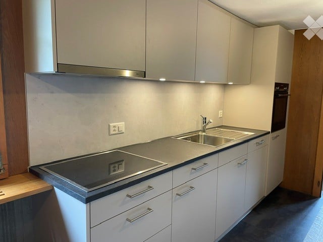 Modern kitchen with white cabinets, induction stove, sink, and oven. Features sleek countertops and built-in lighting.