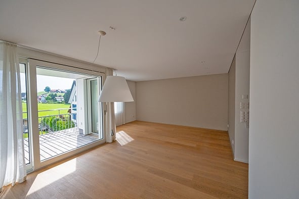 Empty room with wooden flooring, large window leading to a balcony, white walls, and a modern light fixture.