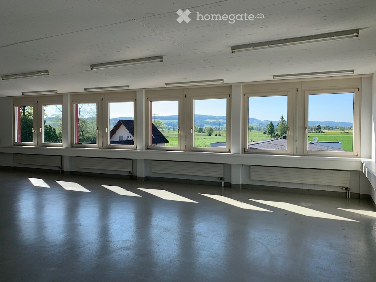 Empty room with large windows, white walls, and a polished concrete floor. No furniture or equipment present.