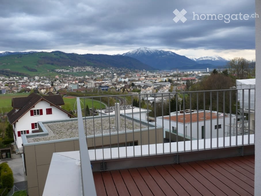 Balcony with wooden decking, metal railing, overlooking a cityscape and mountains.