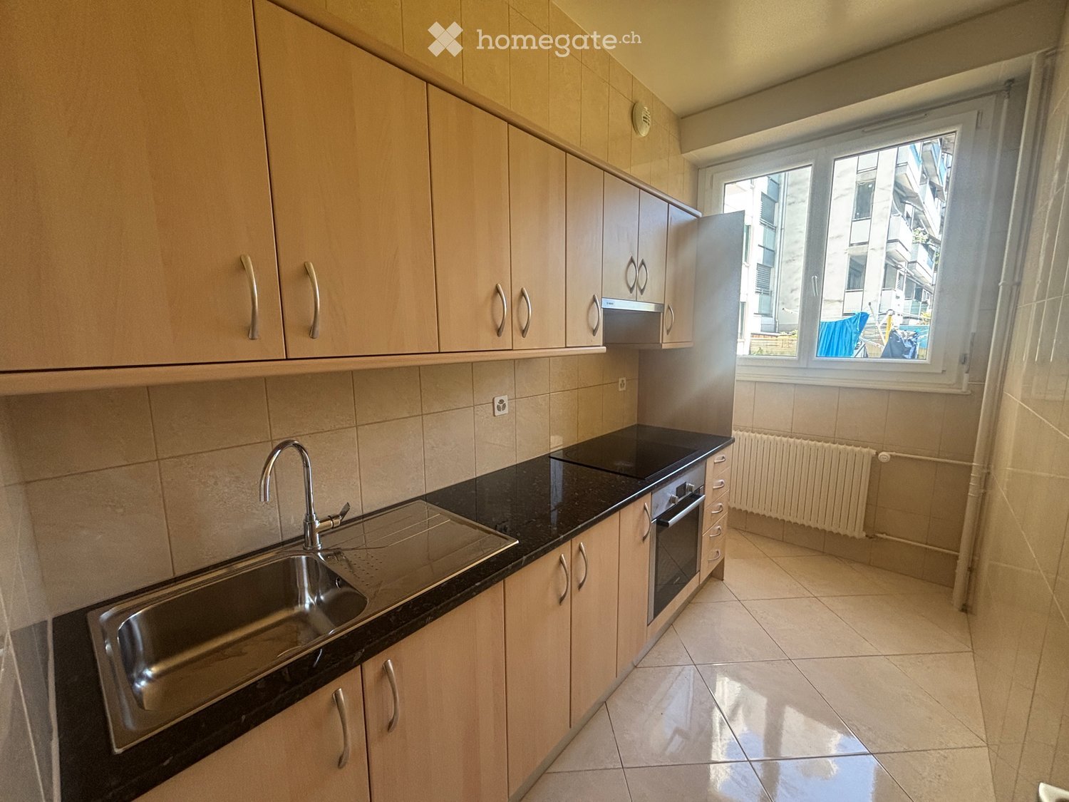 Modern kitchen with light wooden cabinets, black countertop, stainless steel sink, and built-in oven.