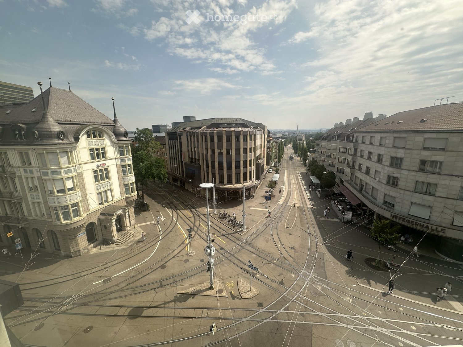 Aerial view of a city street intersection with tram tracks, buildings, and pedestrians.