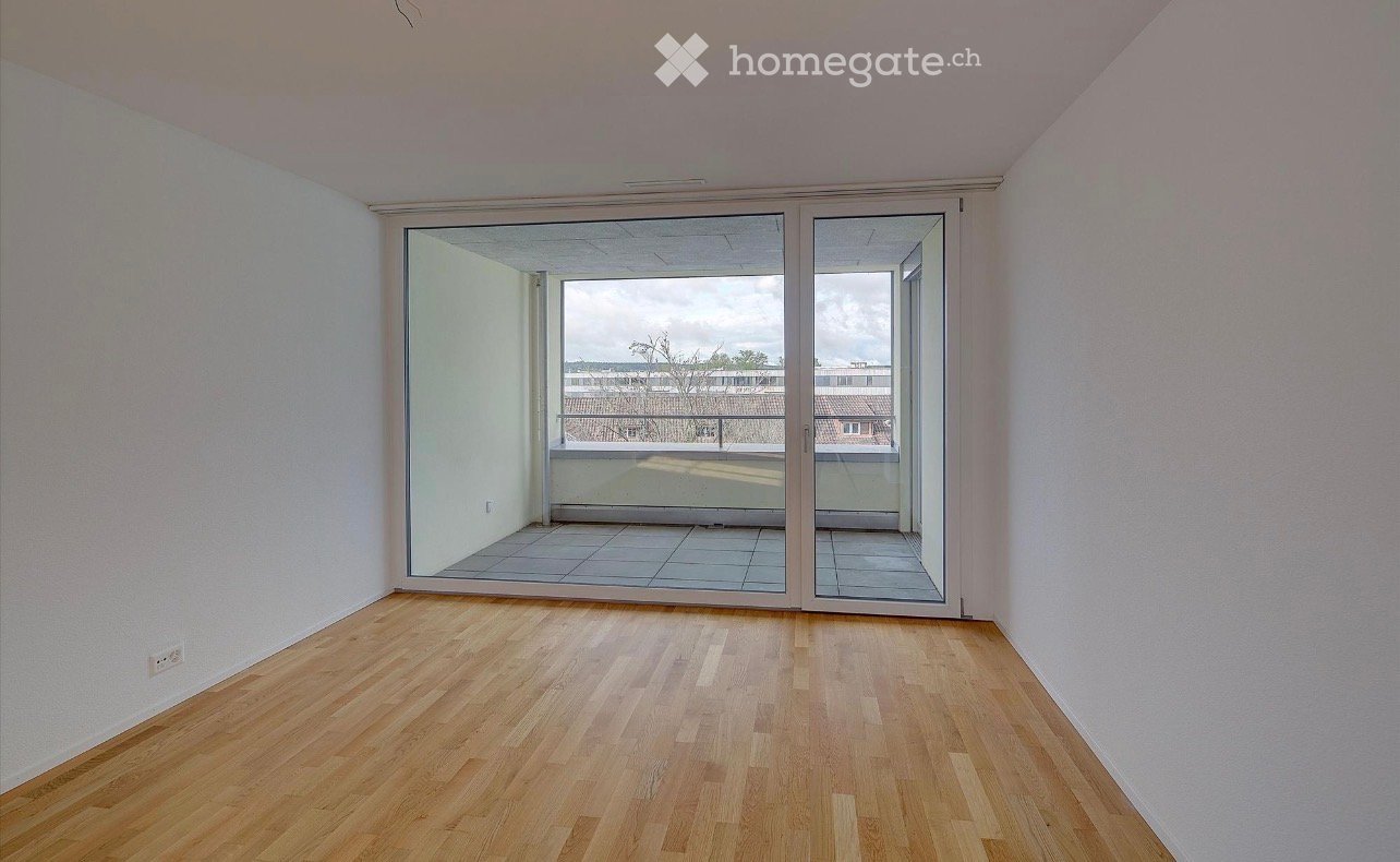 Empty room with wooden flooring, white walls, and large sliding glass doors leading to a balcony.