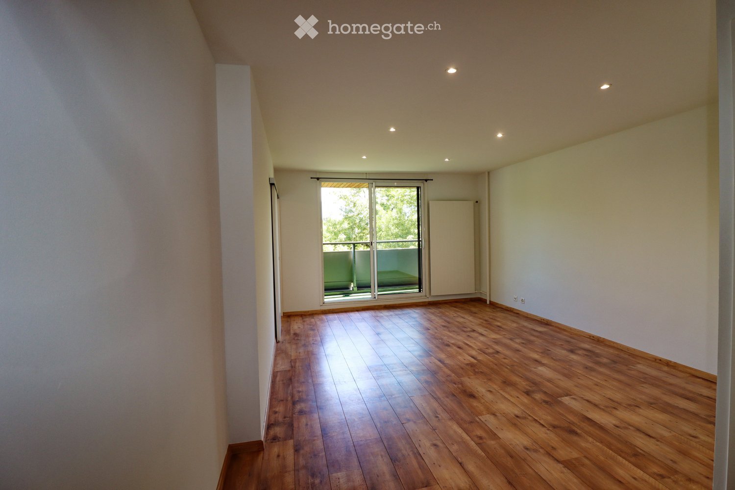 Empty room with wooden flooring, white walls, and a large sliding glass door leading to a balcony.