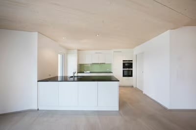 Modern, minimalist kitchen with white cabinetry, black countertops, and a central island. Features a sink and built-in oven.