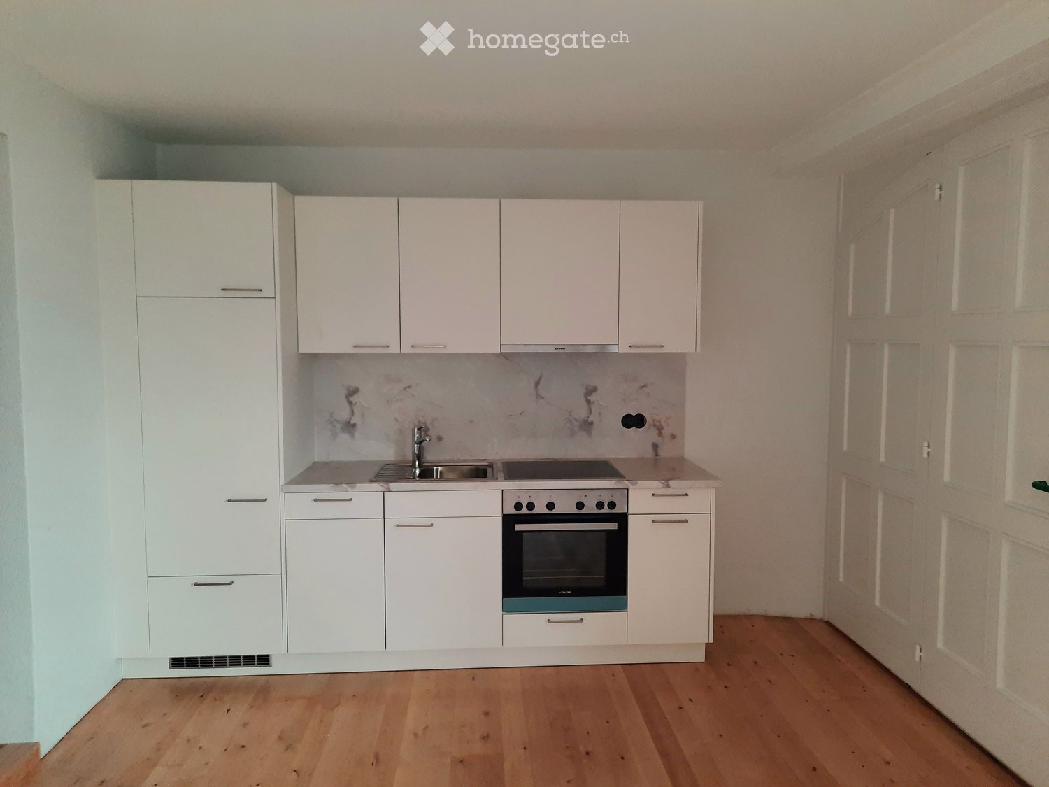 Modern kitchen with white cabinets, a sink, and an oven, featuring a marble backsplash and wooden flooring.