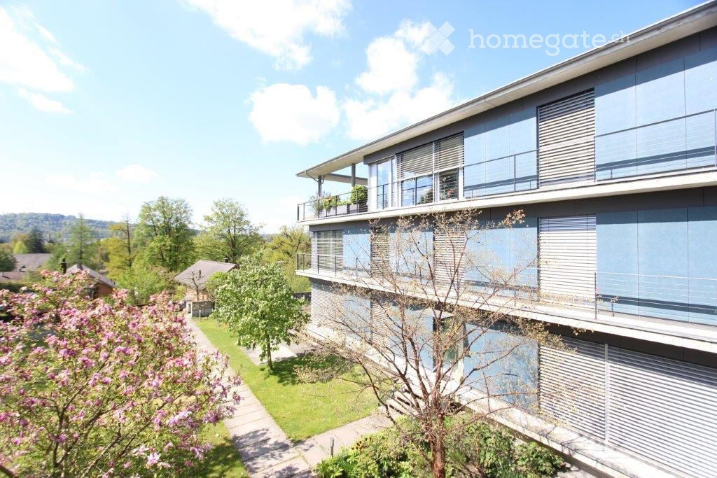 Modern two-story building with large windows and balconies, surrounded by greenery and a well-maintained garden.
