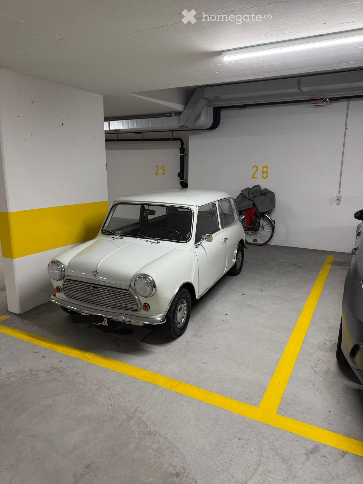 Underground parking area with a white vintage car, bicycle, and numbered parking spots.