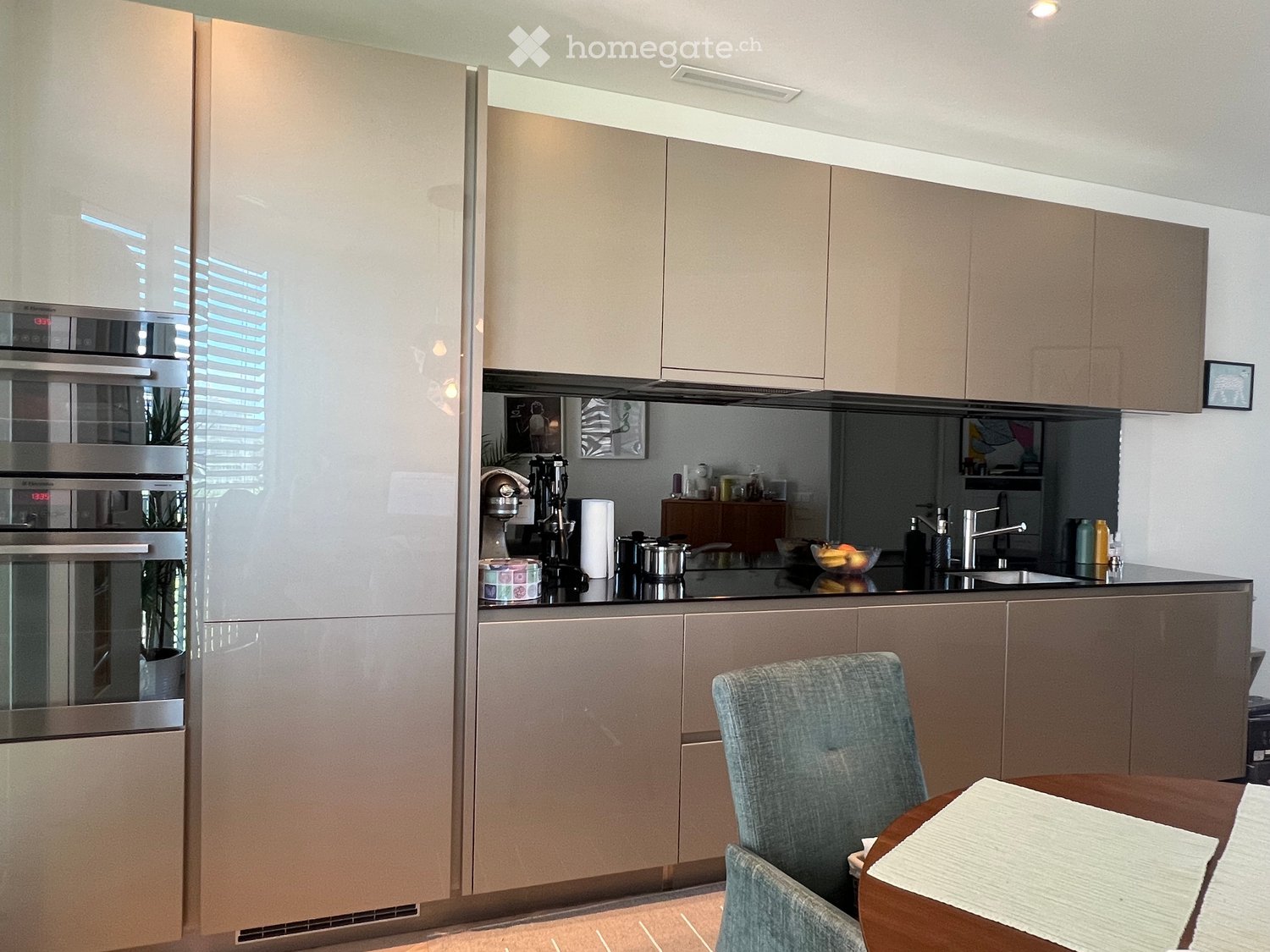 Modern kitchen with light wood cabinets, stainless steel appliances, and a black countertop. Includes a dining area with a table and chairs.