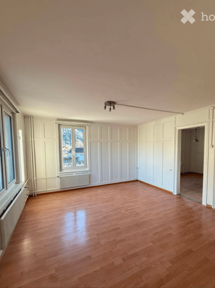 Empty room with wooden flooring, white walls, and large windows offering a view of the outside. No furniture or equipment is present.