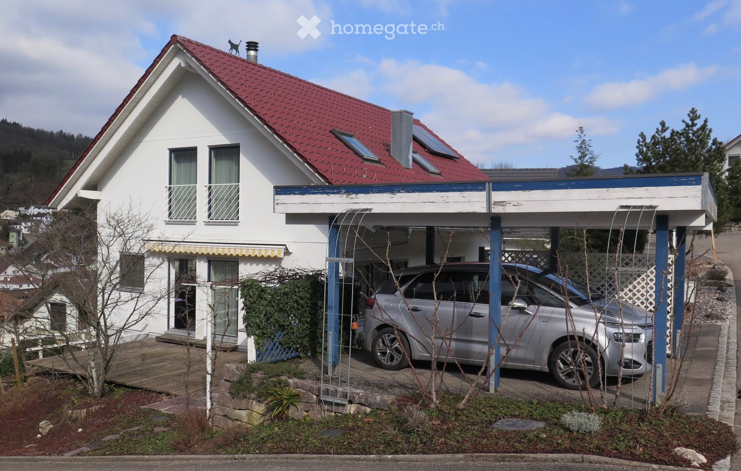Two-story white house with red tile roof, balcony, garage, and parked car.