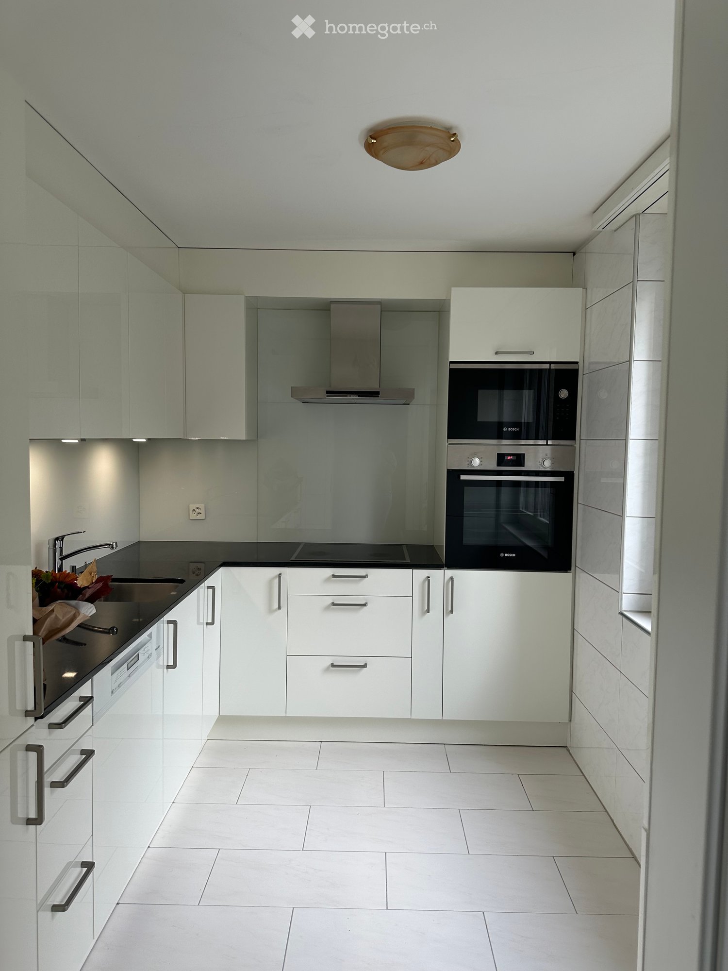 Modern kitchen with white cabinets, stainless steel appliances, and a black countertop. Features include a sink with a faucet, an oven, a microwave, and a decorative flower arrangement on the counter.