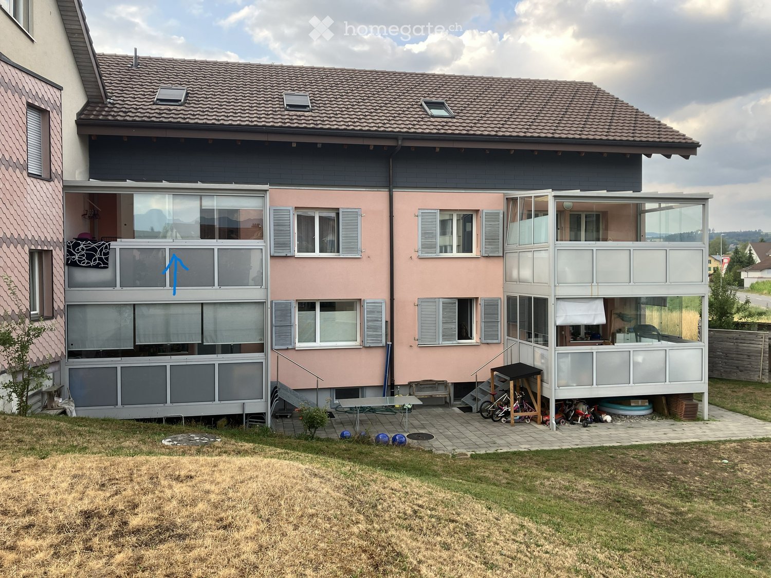 Two-story house with pink and grey exterior, multiple windows, balconies, and a covered patio area with outdoor furniture.