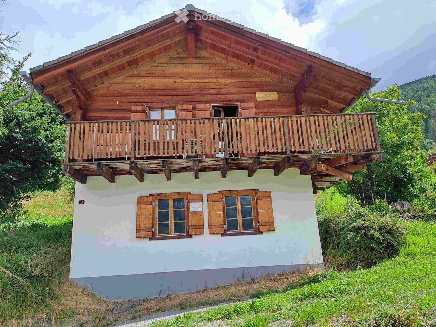 Two-story wooden house with a balcony on the upper level, light green lower facade, and wooden shutters on windows.