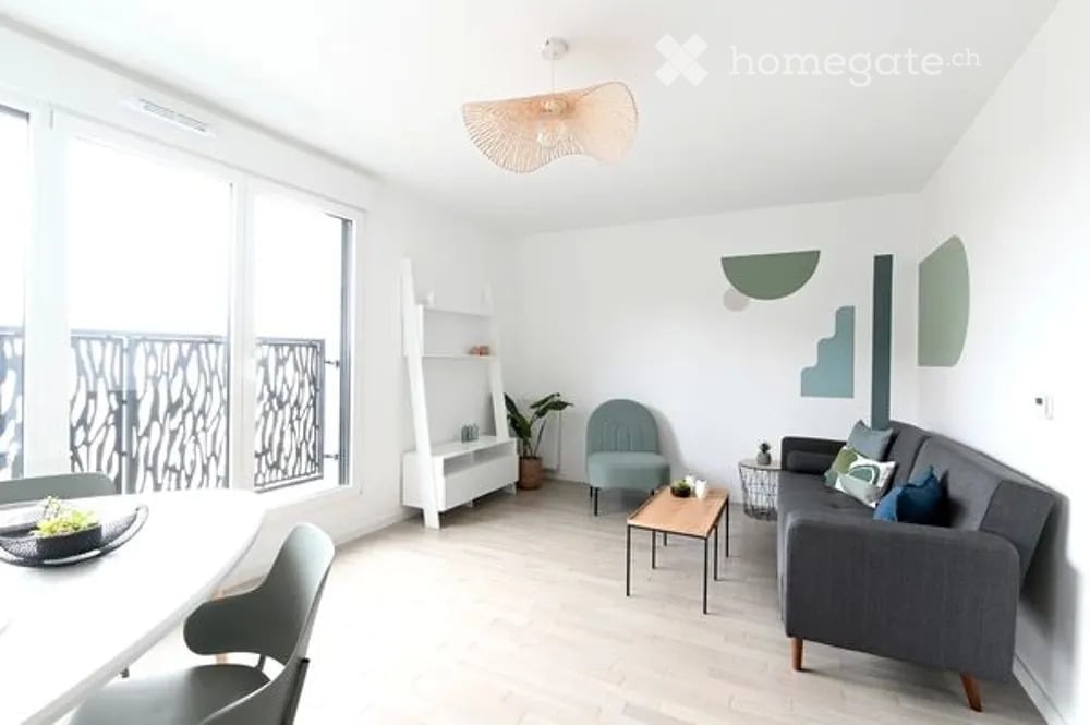 Modern living room with large windows and balcony access, featuring a grey sofa, coffee table, armchair, white shelving unit, and decorative wall art.