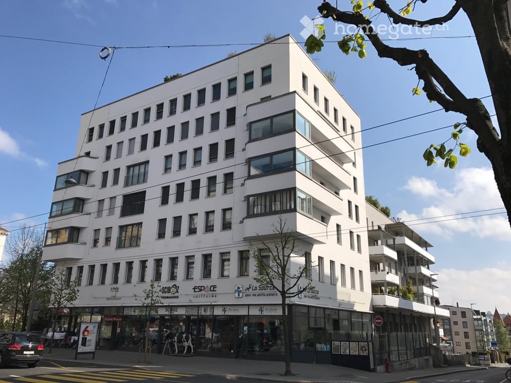 large multi-story building, white exterior, multiple balconies, large windows, shops on ground floor