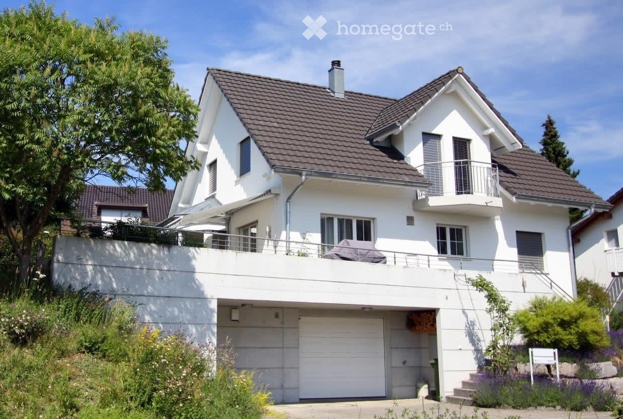 Two-story white house with a brown tiled roof, garage, balcony, and raised ground floor.