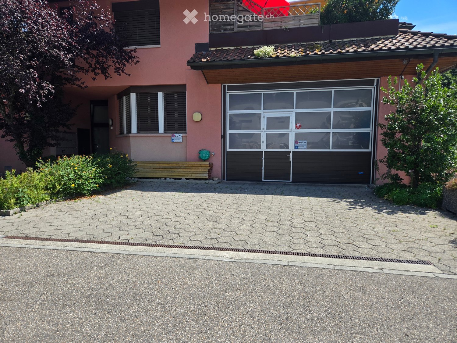 Two-story house with a large garage, pink exterior, and a balcony on the upper floor.