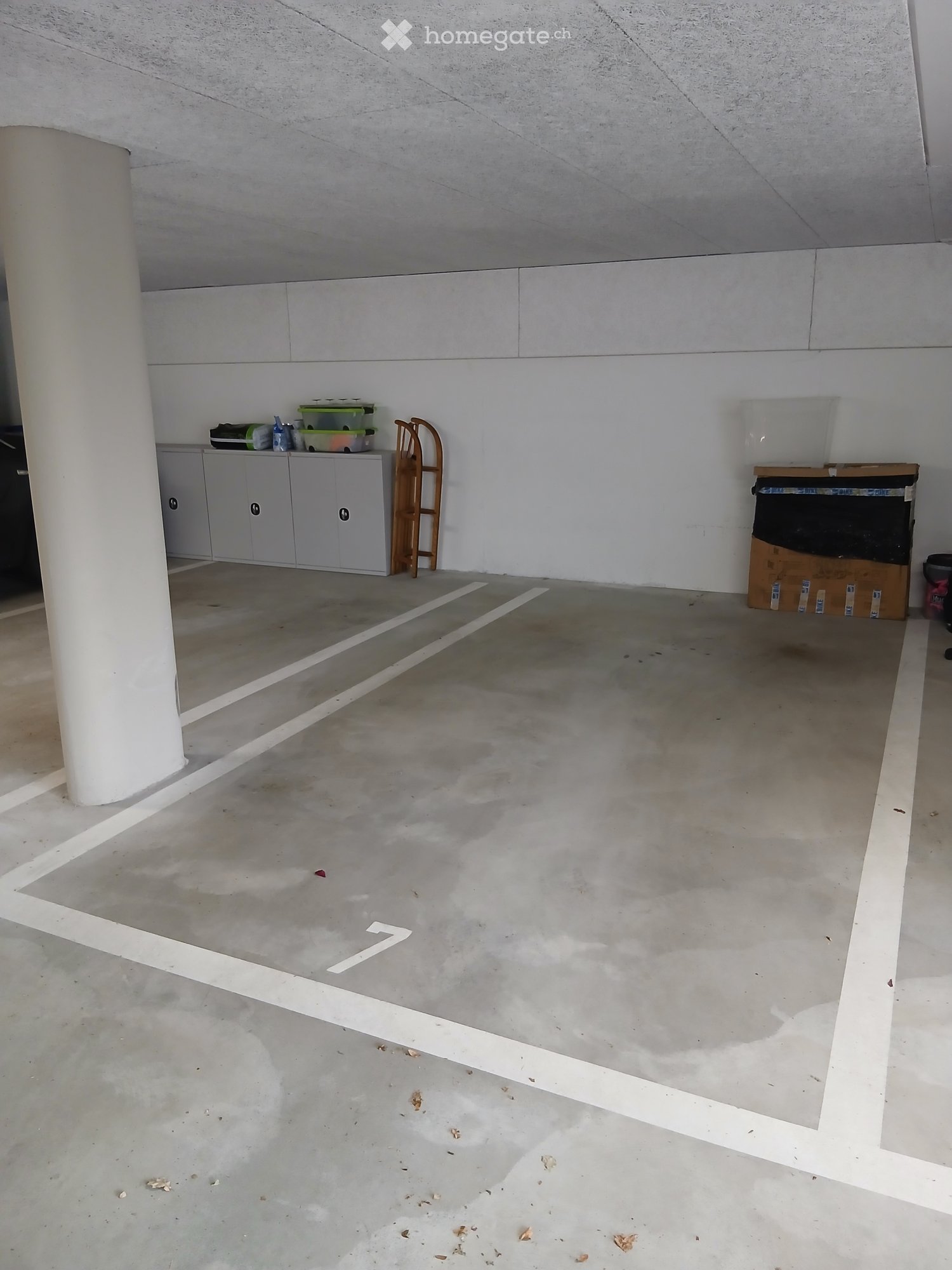 Empty concrete-floored room with white walls, a grey cabinet, and a wooden ladder. The space is clean and unfurnished.
