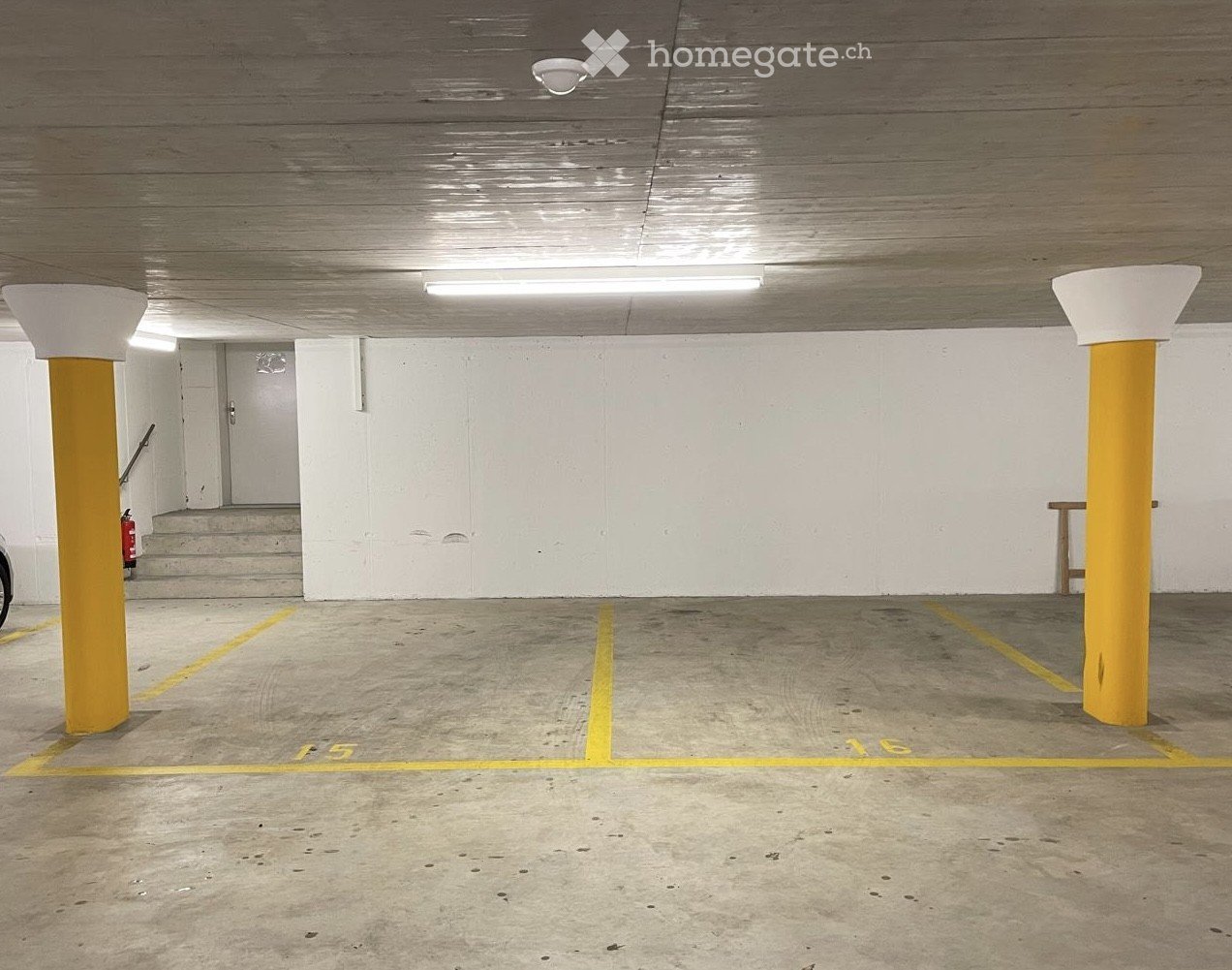 Underground parking area with marked parking spaces, yellow pillars, and a staircase leading upwards.