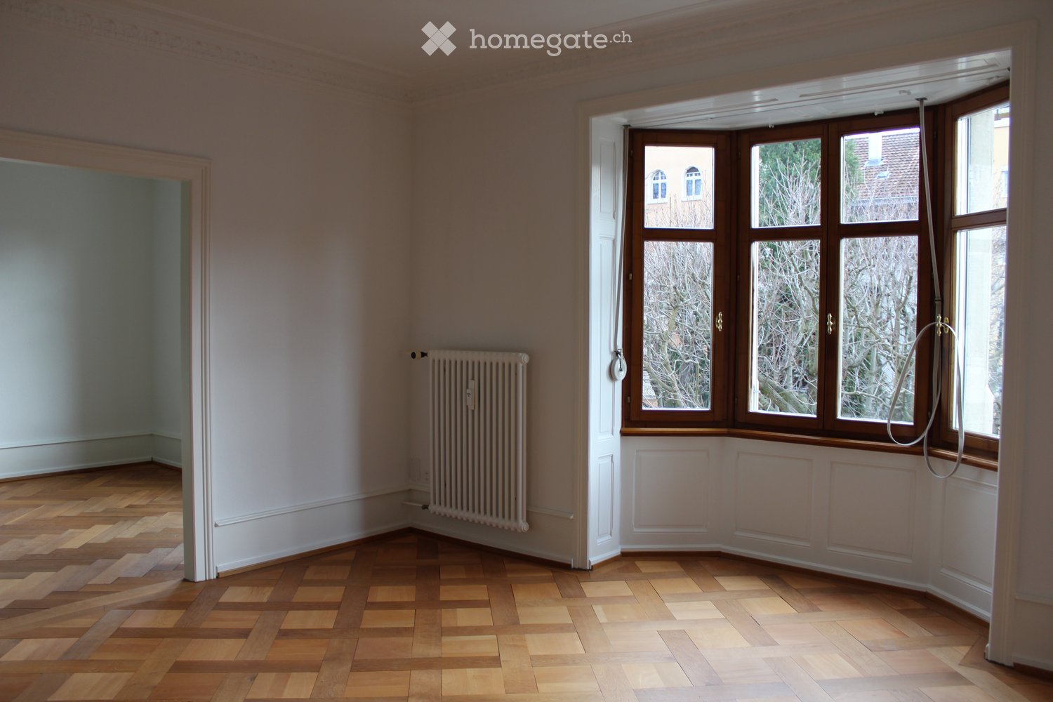 Empty room with wooden flooring, large windows, radiator, and white walls.