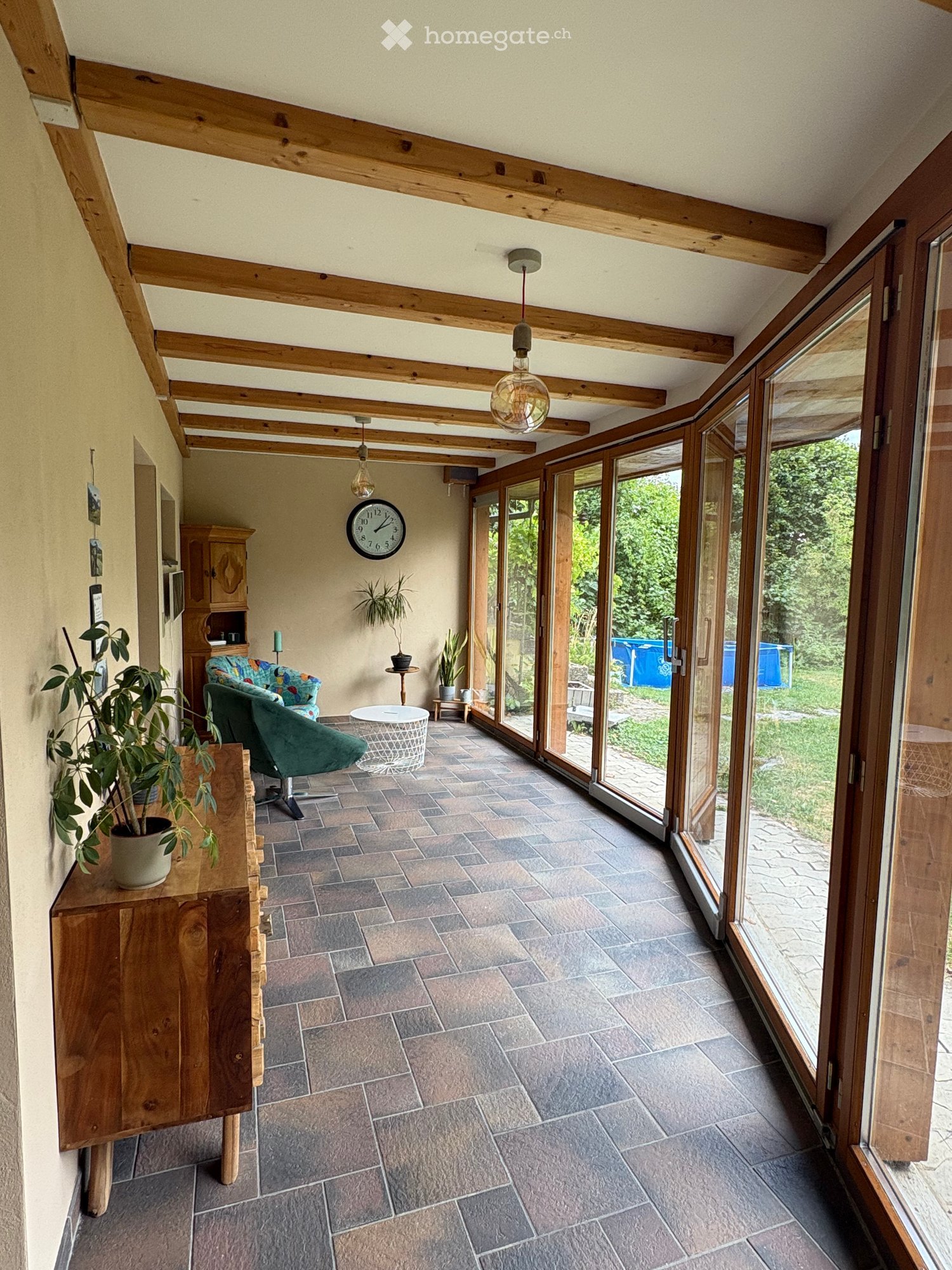 Bright, spacious room with wooden beams, large windows, tiled floor, and comfortable seating area.
