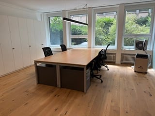 Bright, modern office space with large windows, hardwood flooring, a long conference table, several office chairs, a cabinet, and a printer.