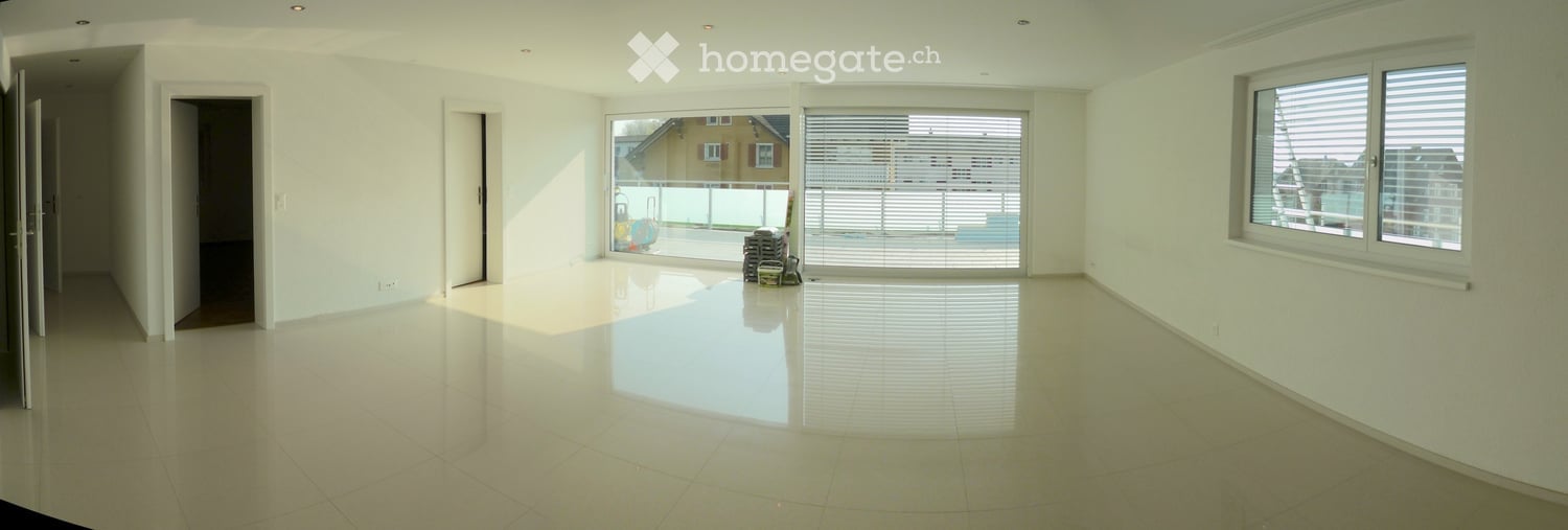 Empty room with white walls, polished tile floor, large windows, and sliding glass doors leading to a balcony area.