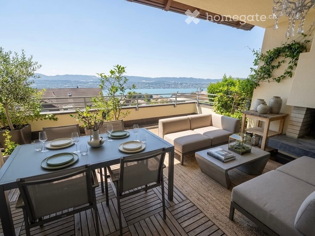 Outdoor terrace with a view of a lake and mountains, featuring a dining table with chairs, a sofa, coffee table, and decorative items.