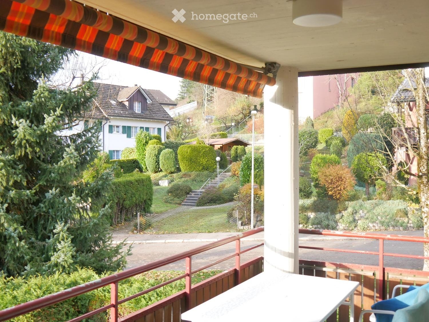Balcony with a table and chair, overlooking a well-maintained garden and residential area.