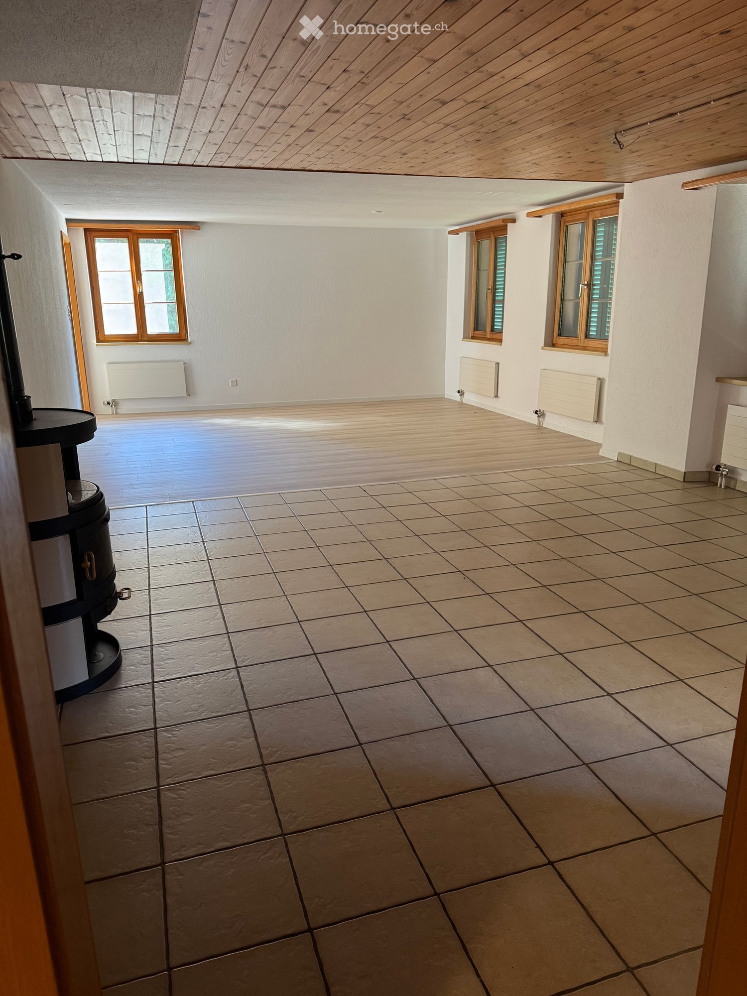 Empty room with wooden ceiling, tiled floor, and wooden-framed windows. No furniture or equipment present.