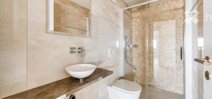 Modern bathroom with a white sink, mirror, toilet, and glass-enclosed shower. Light-colored tiles and sleek fixtures.