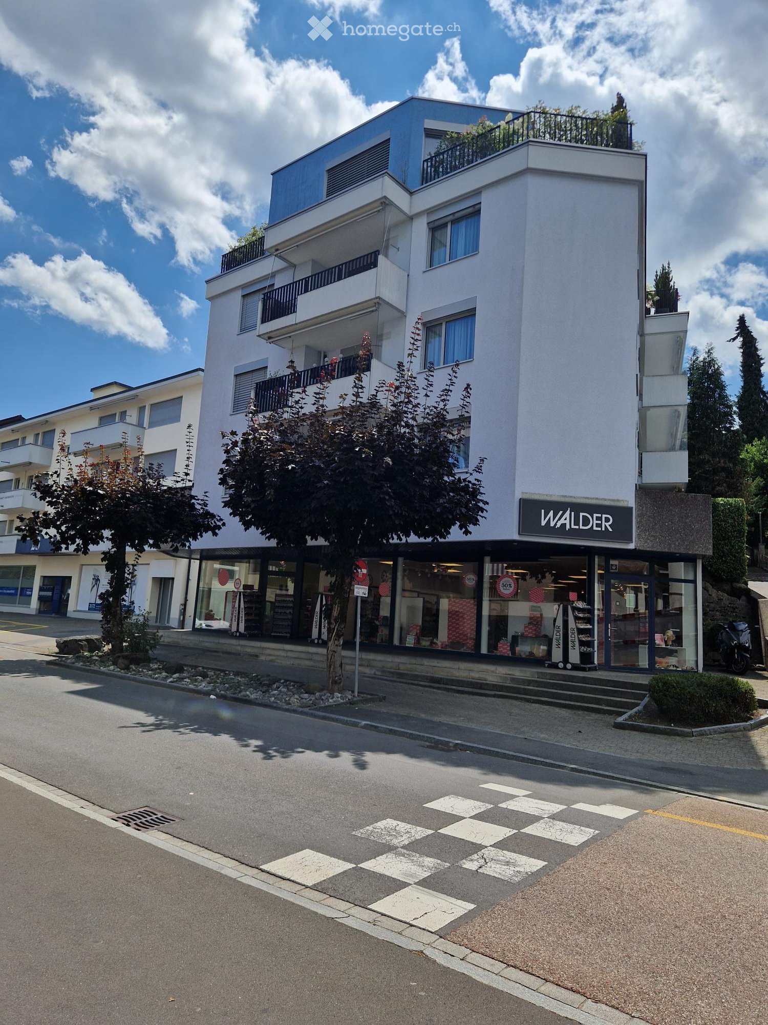 Modern multi-story building with balconies, large windows, and a storefront labeled "WALDER" on the ground floor.
