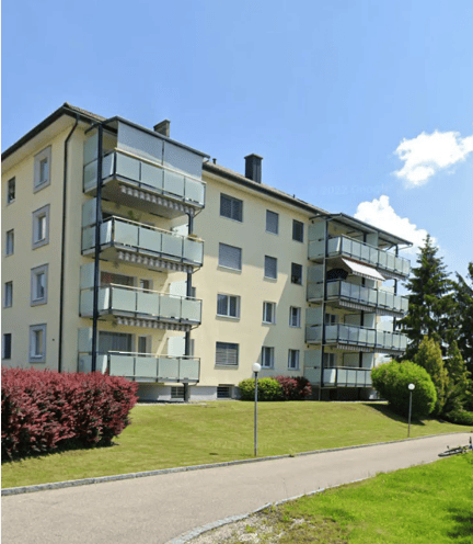 Multi-story residential building with multiple balconies and a well-maintained lawn in front.