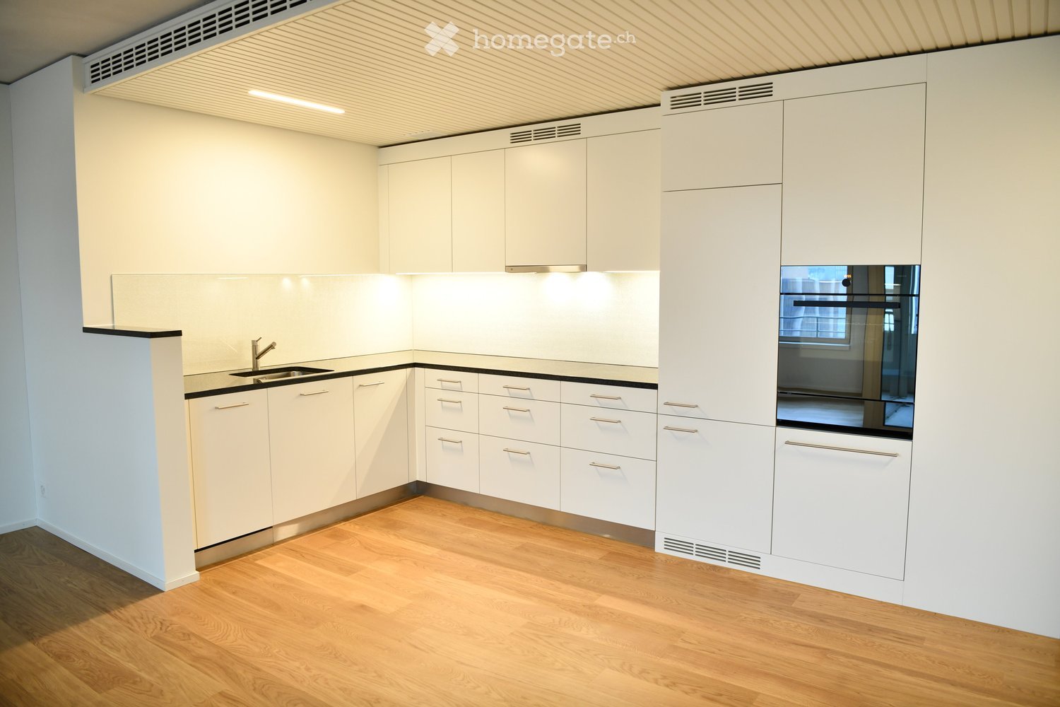 Modern kitchen with white cabinets, wooden flooring, and a stainless steel sink.