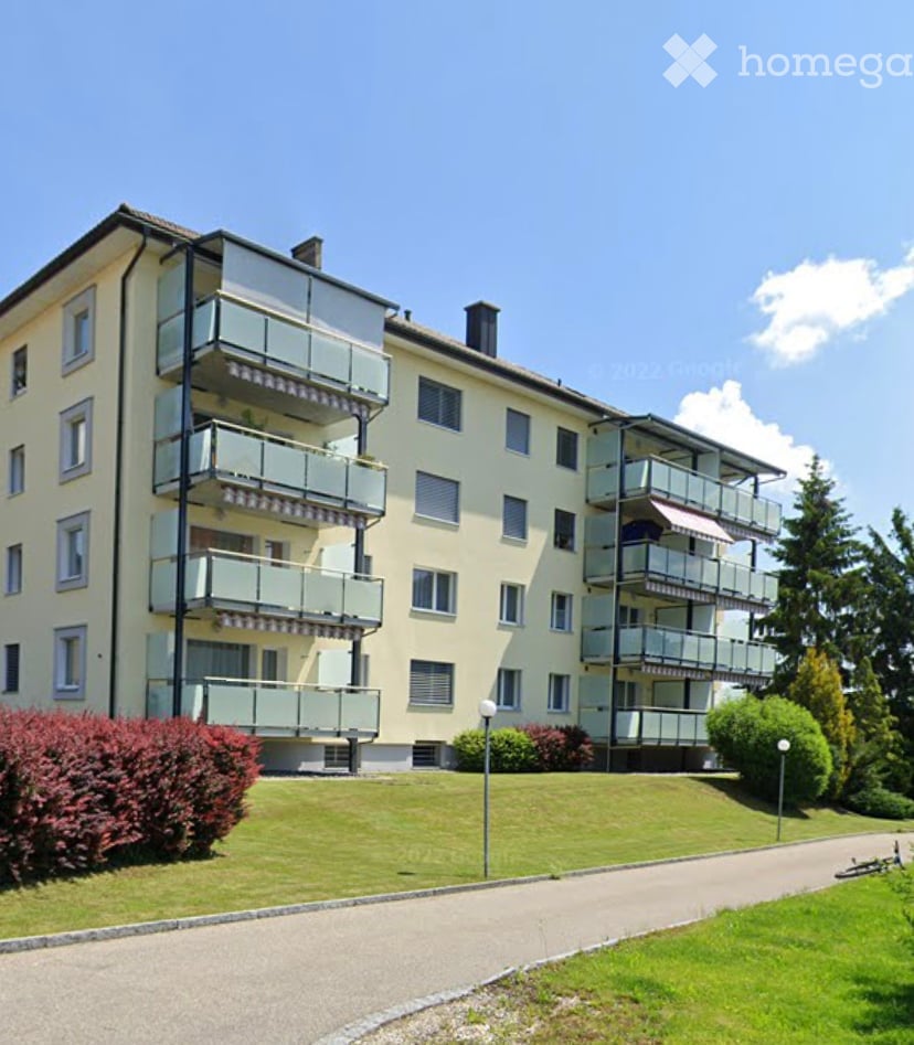 Multi-story residential building with multiple balconies and a well-maintained lawn in front.